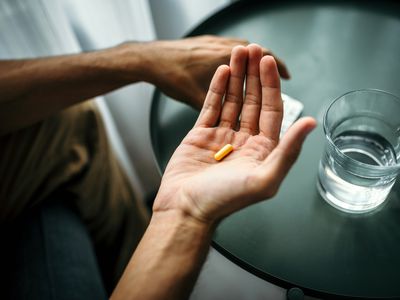 Hand holding a pill in front of a table with a glass of water