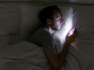 Man looking at smartphone while lying in bed at night