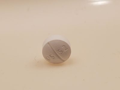 Close-up of a white oxycodone hydrochloride 5 mg pill, marked as 05 52, resting on its edge