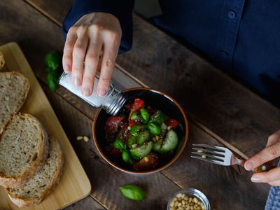 Vegetable salad of tomatoes, cucumbers, nuts and seeds, Green Basil Leaves, and Salts It From a salt Shaker. Next To It Are Sliced Baguette Slices.