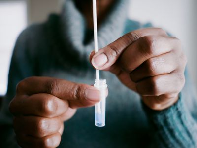 Close-up of unrecognizable black woman swirling nasal swab in reagent solution for at-home COVID test