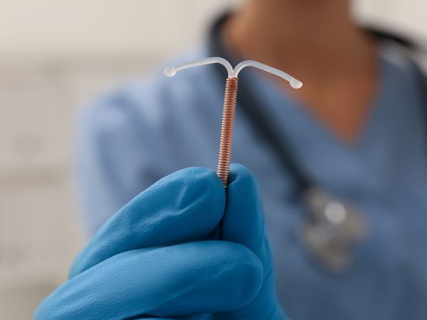 Doctor holding T-shaped intrauterine birth control device on blurred background, closeup