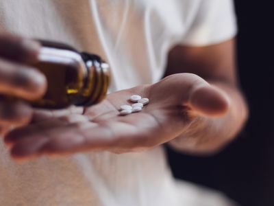 Person spilling pills out in the palm of their hand from a pill bottle