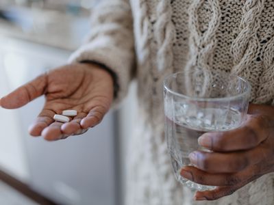 Close-up of unrecognizable person holding pills and glass of water