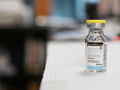 A close up of a bottle of ketamine solution on a white table with a blurred background