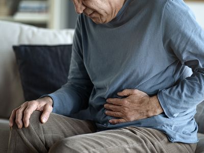 Older man holding hand to stomach while sitting on a couch