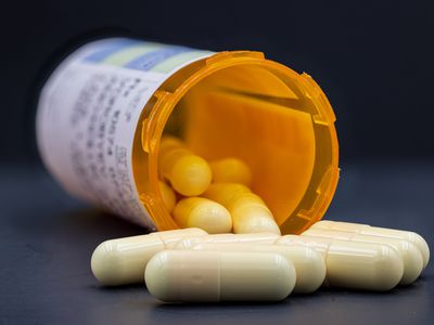 Closeup of white pills spilling out of orange prescription pill bottle.