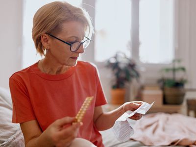 Older woman reading prescription medication instructions in her bedroom while holding a blister pack of pills