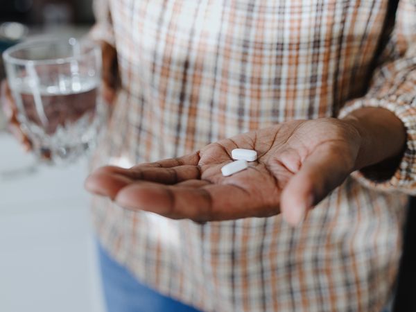 Close-up of person holding two pills in one hand and glass of water