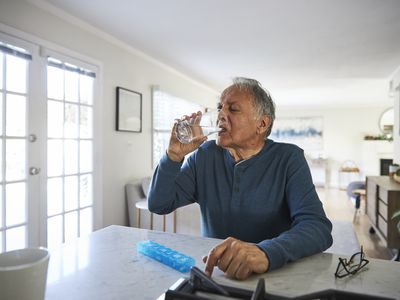 Senior man drinking a glass of water with a pillbox sitting in front of him on the counter