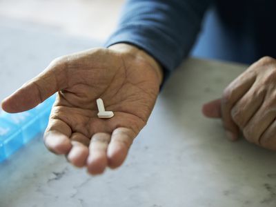 Close up of an older person's hand holding pills with a pill box on the counter