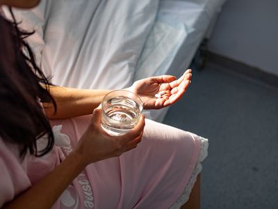 A woman sitting on a bed with pills and a glass of water in her hand