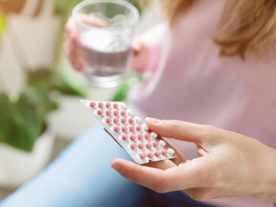 Woman holding contraceptive pills in blister pack and glass of water