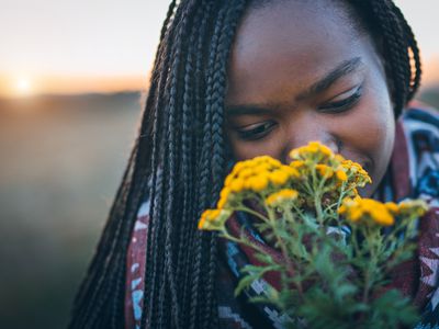 A Black woman holds a bouquet of flowers with her nose close to them