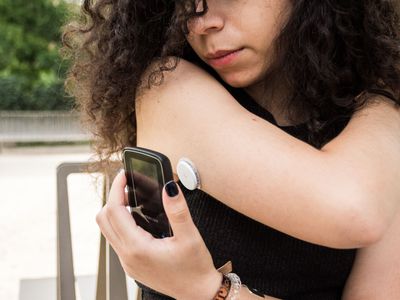 Female equipped with glucose sensor on back of arm and scanner measuring blood sugar levels