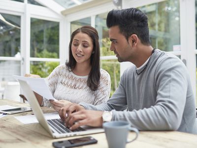 Woman showing document to man using laptop