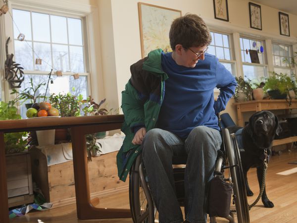 A woman in a wheelchair putting on coat, with support dog